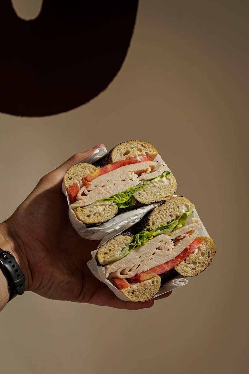 Day Shift bagel — turkey, lettuce, tomato with cranberry mayo, held up to camera.