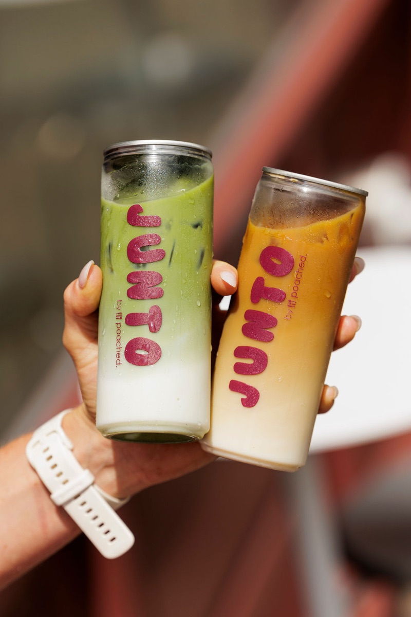 Both JUNTO cans held up, dew on the glass, natural daylight.