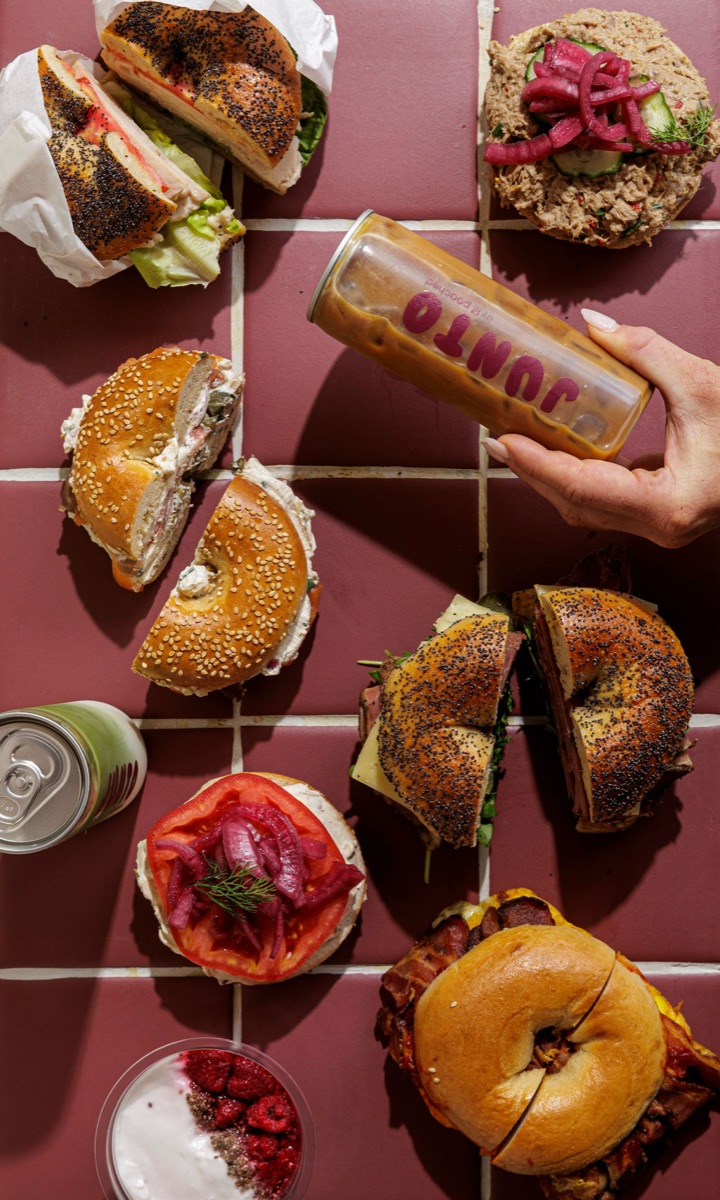 Overhead flat lay of Junto bagels with a hand placing a JUNTO iced coffee can.