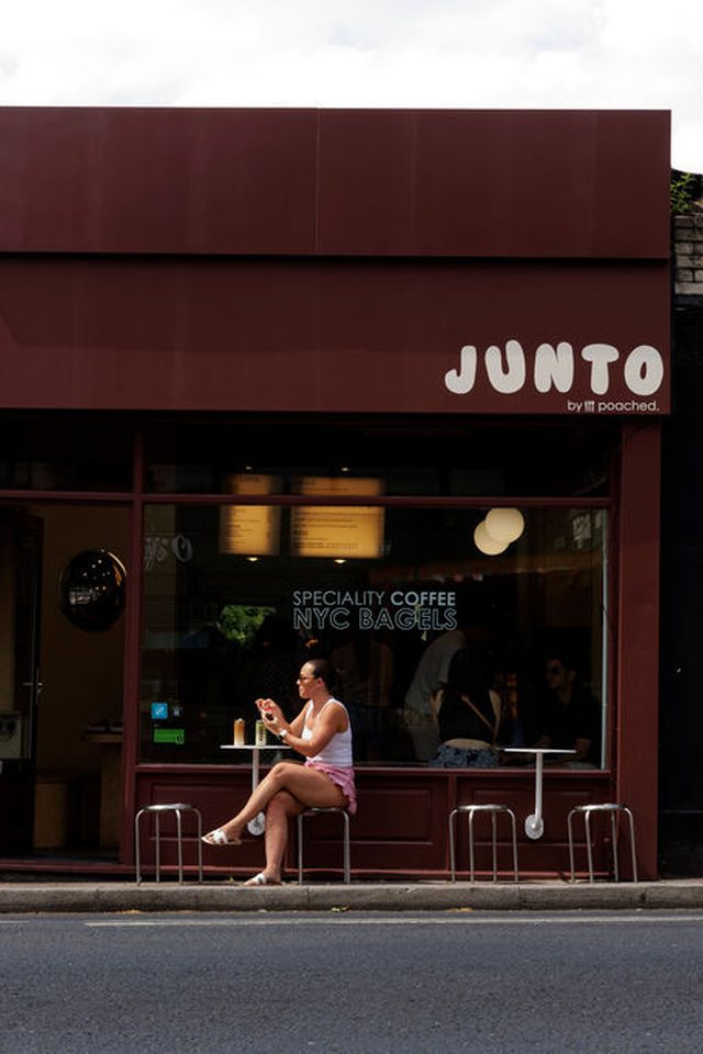JUNTO by Poached shopfront on Beckenham High Street between the shoe repairs shop and Airbnb — a customer sits at the window bench.